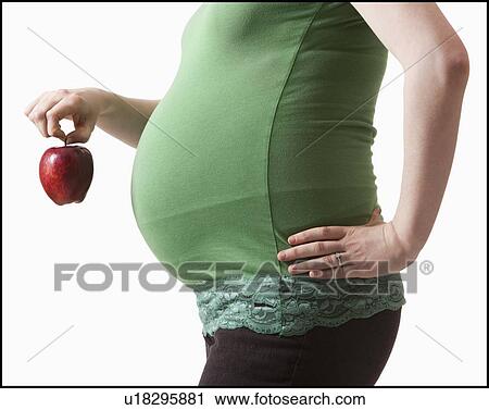 Stock Image - Pregnant woman holding red apple. Fotosearch