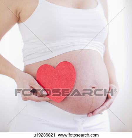 Pregnant woman holding red paper heart on her belly View Large Photo Image Stock Image - Pregnant woman holding red paper heart on her belly. Fotosearch