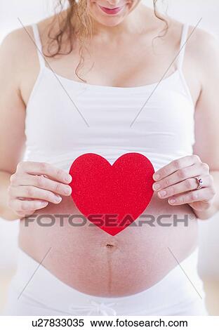 Pregnant woman holding red paper heart on her belly View Large Photo Image Stock Photography - Pregnant woman holding red paper heart on her belly. Fotosearch