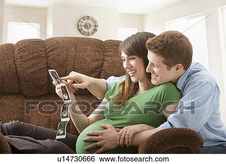 Stock Photograph - Pregnant woman with boyfriend watching ultrasonography scan. Fotosearch