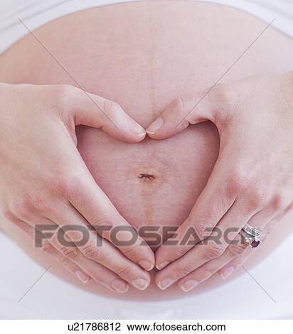 Stock Image - Pregnant woman with hands folded as heart on her belly. Fotosearch