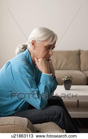 Stock Image - Sad senior woman sitting on armchair. Fotosearch