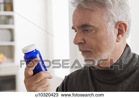 Stock Image - Senior men reading label on medicine bottle. Fotosearch