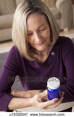 Stock Image - Senior woman reading label on medicine bottle. Fotosearch