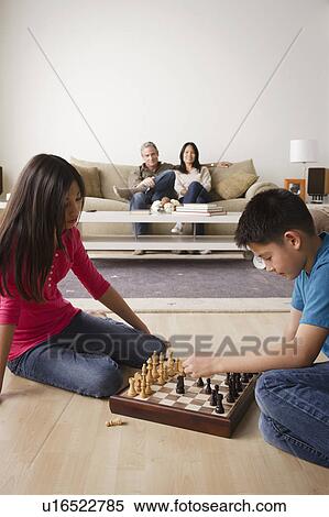 Stock Photography - Siblings playing chess game while parents watching from sofa. Fotosearch