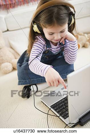 Stock Image - Small girl (4-5 years) listening to music from laptop. Fotosearch