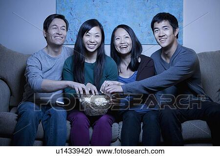 Stock Image - Smiling family watching TV and eating popcorn. Fotosearch