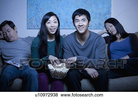 Stock Photo - Smiling family watching TV and eating popcorn. Fotosearch