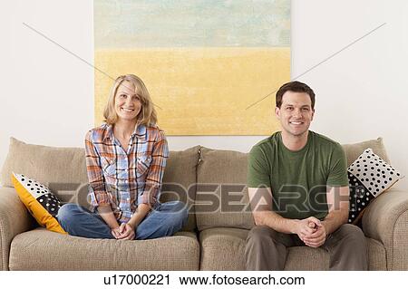 Stock Image - Smiling mid adult couple sitting on sofa. Fotosearch