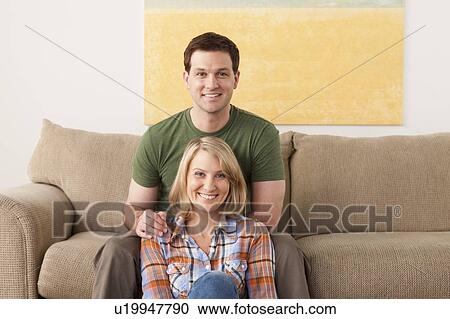 Stock Image - Smiling mid adult couple sitting on sofa. Fotosearch