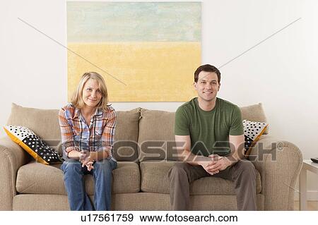 Smiling mid adult couple sitting on sofa View Large Photo Image Stock Photo - Smiling mid adult couple sitting on sofa. Fotosearch
