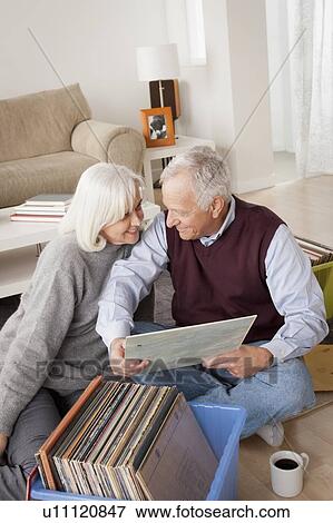 Stock Photo - Smiling senior couple looking at vinyl's in living room. Fotosearch