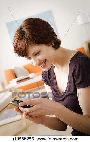 Stock Photograph - Smiling woman using mobile at home. Fotosearch