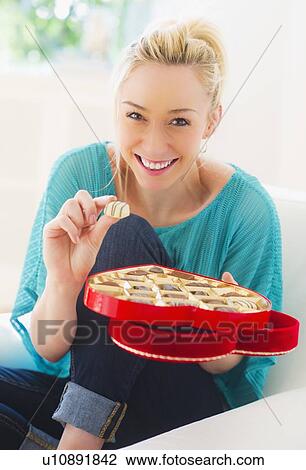 Stock Image - Smiling young woman eating chocolates. Fotosearch