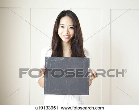 Stock Image - Smiling young woman holding black board. Fotosearch