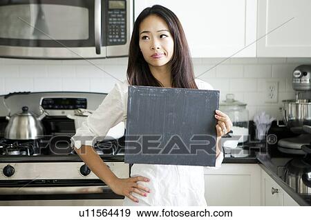 Smiling young woman holding black board in kitchen View Large Photo Image Stock Photo - Smiling young woman holding black board in kitchen. Fotosearch