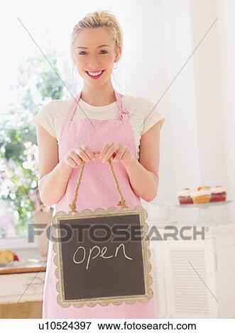Smiling young woman in apron holding open sign View Large Photo Image Stock Photo - Smiling young woman in apron holding open sign. Fotosearch