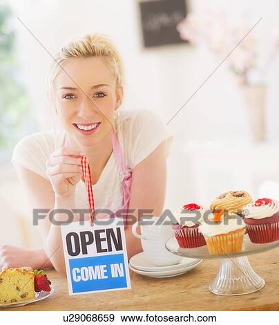 Smiling young woman in apron holding open sign View Large Photo Image Stock Photo - Smiling young woman in apron holding open sign. Fotosearch