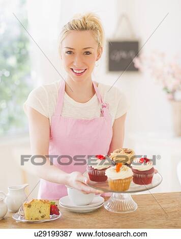 Smiling young woman in apron holding cake stand View Large Photo Image Stock Photo - Smiling young woman in apron holding cake stand . Fotosearch
