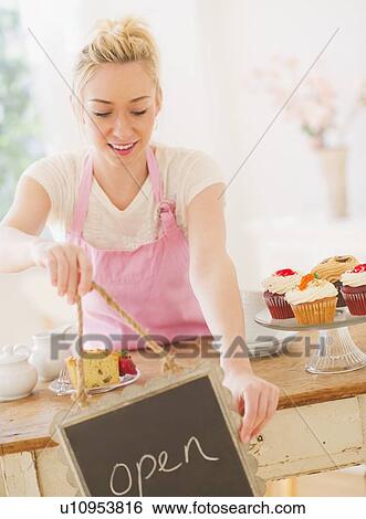 Smiling young woman in apron holding open sign View Large Photo Image Stock Photograph - Smiling young woman in apron holding open sign. Fotosearch