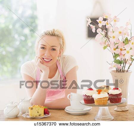 Smiling young woman in apron leaning on table with cakes View Large Photo Image Stock Image - Smiling young woman in apron leaning on table with cakes. Fotosearch