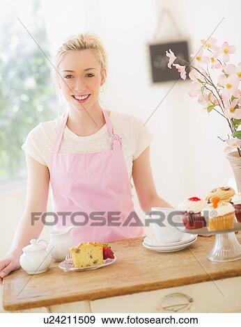 Smiling young woman in apron standing at table with cakes View Large Photo Image Stock Photo - Smiling young woman in apron standing at table with cakes. Fotosearch