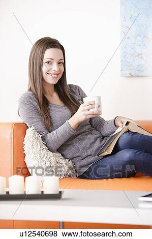 Smiling young woman reading on sofa View Large Photo Image Stock Photo - Smiling young woman reading on sofa. Fotosearch