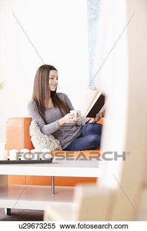 Stock Photography - Smiling young woman reading on sofa. Fotosearch