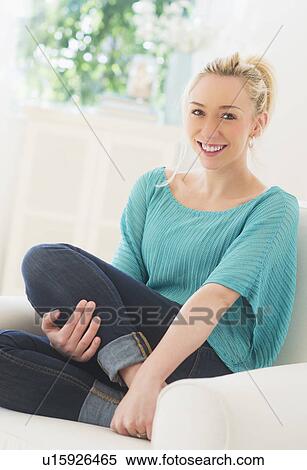 Stock Photography - Smiling young woman sitting on sofa. Fotosearch