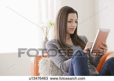 Smiling young woman using digital tablet on sofa View Large Photo Image Stock Image - Smiling young woman using digital tablet on sofa. Fotosearch