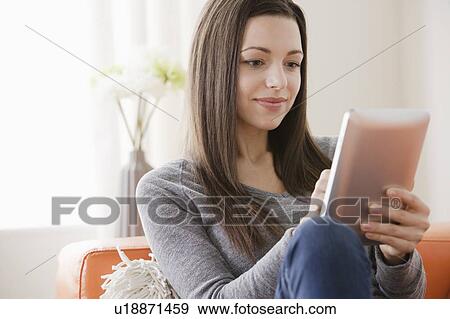 Stock Photo - Smiling young woman using digital tablet on sofa. Fotosearch