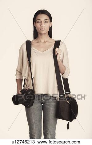 Stock Image - Studio portrait of woman carrying camera with bag. Fotosearch