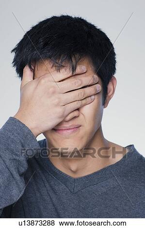 Stock Photo - Studio portrait of young man covering eyes. Fotosearch