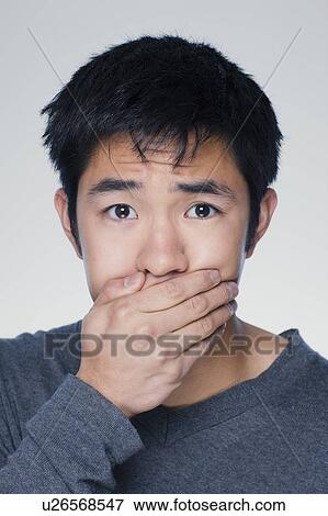 Stock Photo - Studio portrait of young man covering mouth. Fotosearch
