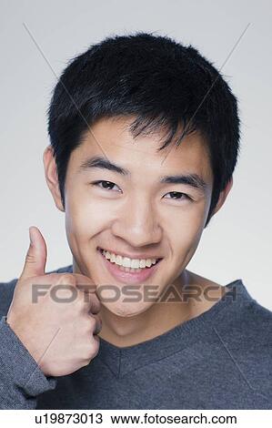 Stock Image - Studio portrait of young man showing thumbs up sign. Fotosearch