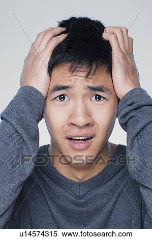 Stock Photography - Studio portrait of young man with head in hands. Fotosearch