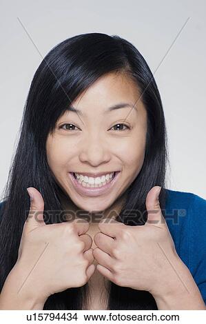 Picture - Studio portrait of young woman showing thumbs up sign. Fotosearch
