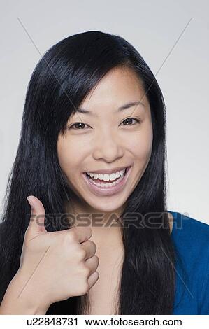 Stock Image - Studio portrait of young woman showing thumbs up sign. Fotosearch