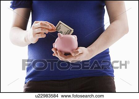 Studio Shot of mid section of pregnant woman putting money into Piggy Bank View Large Photo Image Picture - Studio Shot of mid section of pregnant woman putting money into Piggy Bank. Fotosearch