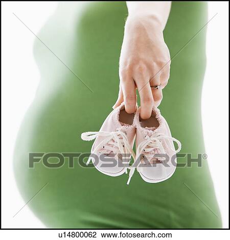Stock Image - Studio Shot of mid section of pregnant woman holing baby booties. Fotosearch