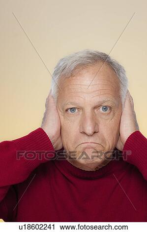 Stock Image - Studio shot of senior man covering ears. Fotosearch