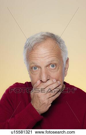 Stock Image - Studio shot of senior man covering lips. Fotosearch