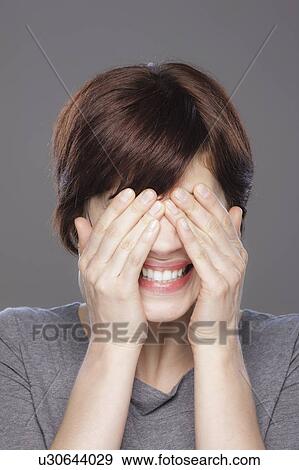 Stock Photo - Studio shot of young smiling woman covering face with hands. Fotosearch