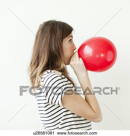 Stock Image - Studio shot of young woman blowing balloon. Fotosearch