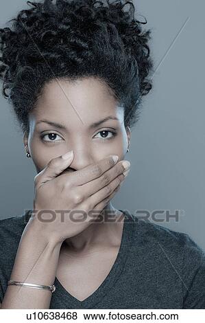 Studio shot of young woman covering lips View Large Photo Image Stock Photo - Studio shot of young woman covering lips. Fotosearch