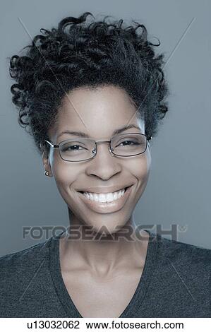 Stock Image - Studio shot of young woman smiling wearing glasses. Fotosearch