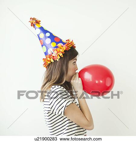 Studio shot of young woman wearing party hat and blowing balloon View Large Photo Image Stock Image - Studio shot of young woman wearing party hat and blowing balloon. Fotosearch