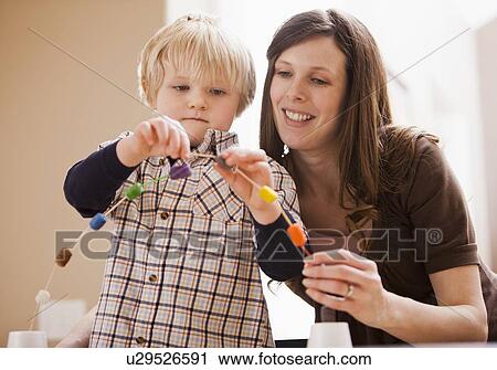 Stock Image - Teacher assisting boy (4-5) in creating chain of beads. Fotosearch