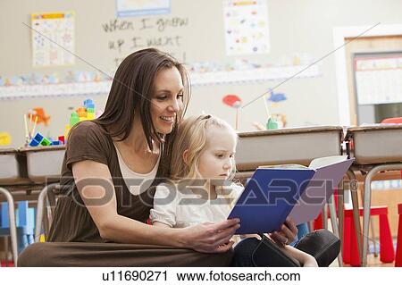 Stock Image - Teacher with girl (4-5) reading book. Fotosearch