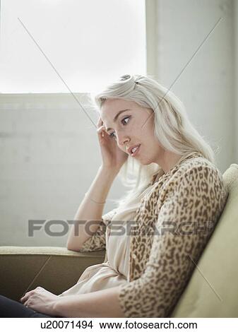 Picture - Thoughtful young woman sitting on sofa. Fotosearch